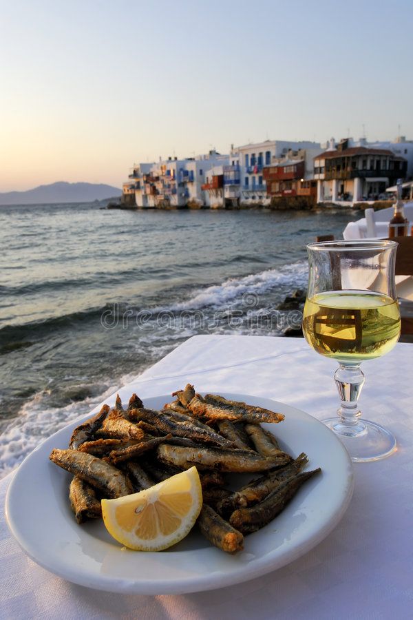 a white plate topped with fried fish next to a glass of wine on top of a table