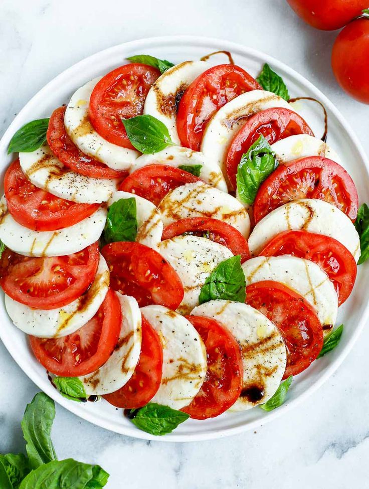 a black plate topped with sliced tomatoes and mozzarella on top of a white table cloth