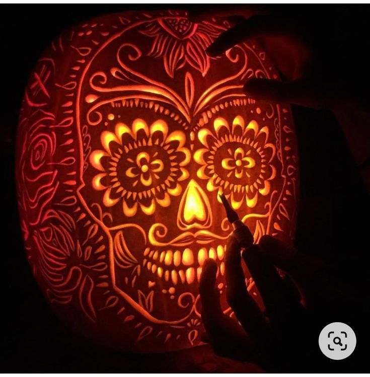 a person carving a pumpkin into the shape of a skull with intricate designs on it