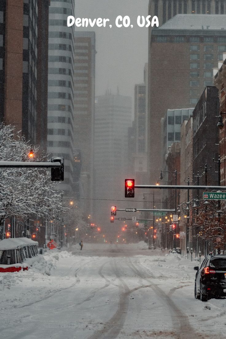 a snowy city street with traffic lights and cars driving down it's side in the snow