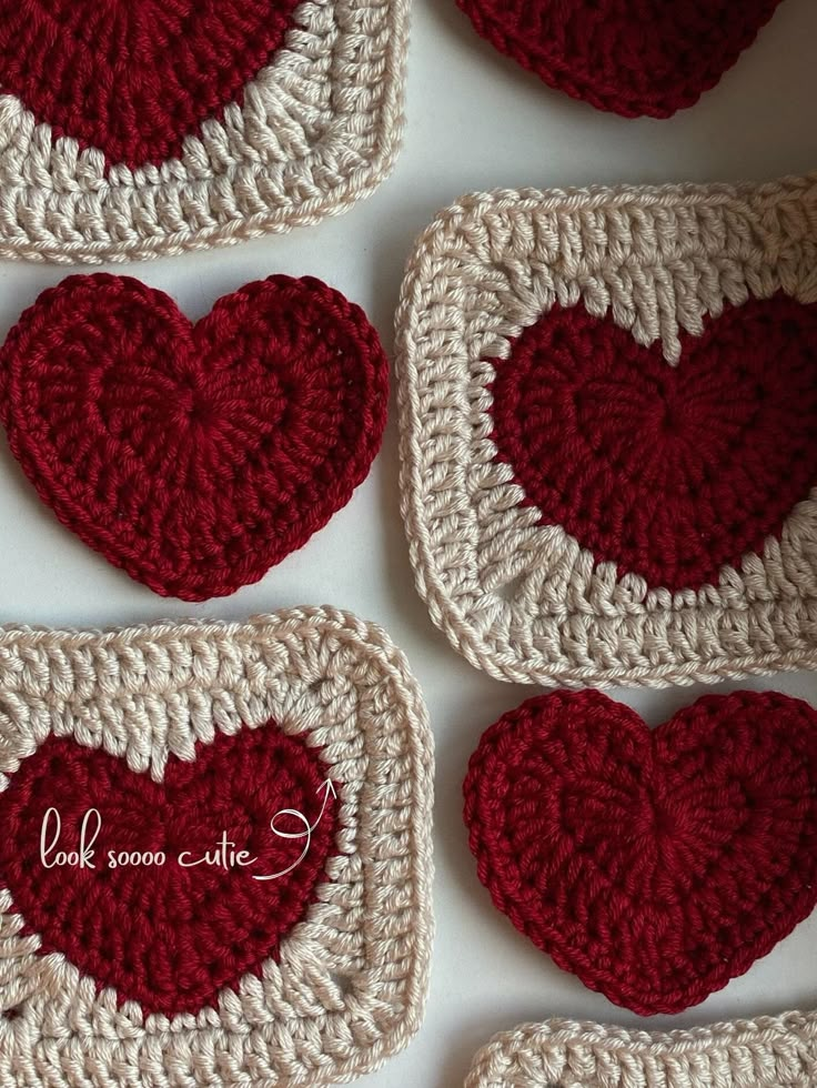 four crocheted heart coasters are arranged on a white surface with red hearts