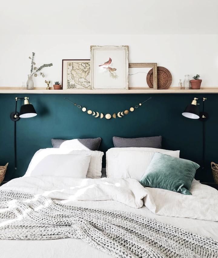 a bed with pillows and blankets on it in front of a wall mounted shelf above the headboard