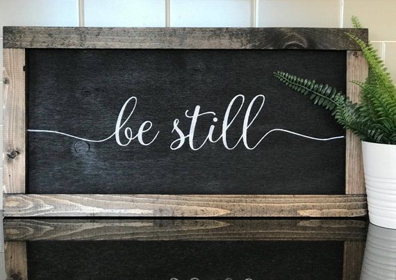 a wooden sign that says be still next to a potted plant