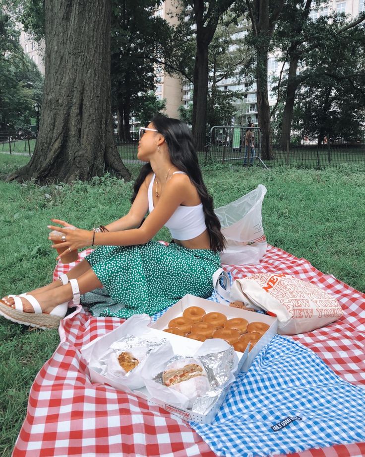 a woman sitting on top of a red and white checkered blanket next to food