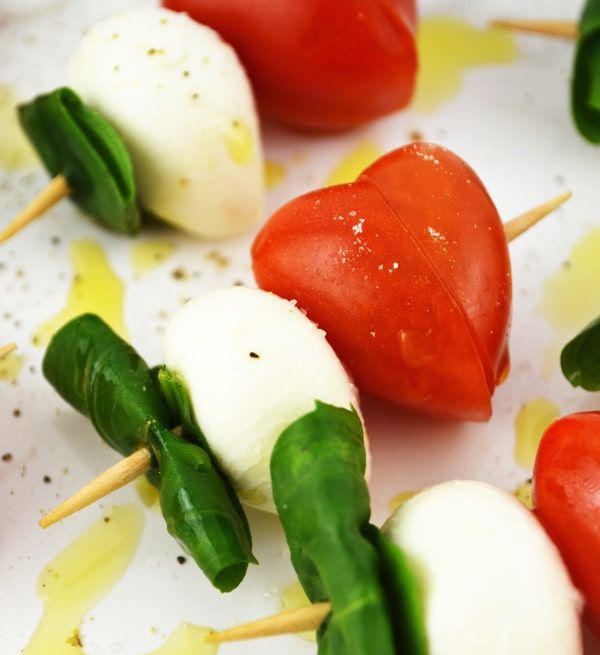 small skewers with tomatoes, mozzarella and spinach leaves on them