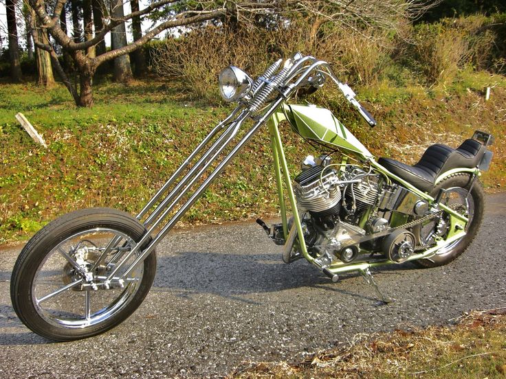 a green motorcycle parked on the side of a road next to a wooded area with trees