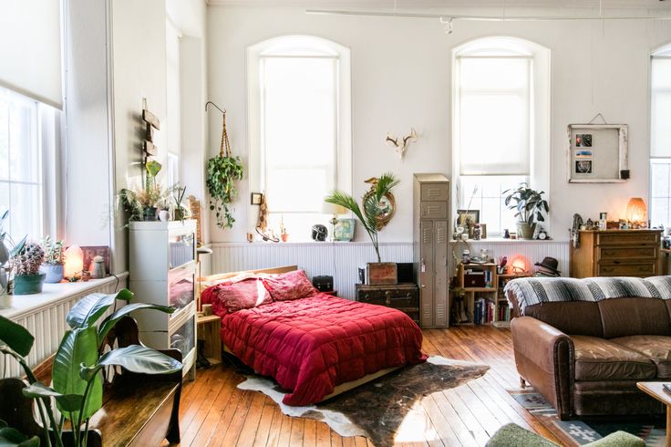 a bed sitting in a bedroom next to two windows with potted plants on them