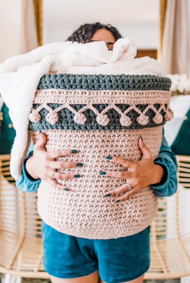 a woman is holding a crocheted basket in her hands and covering her face