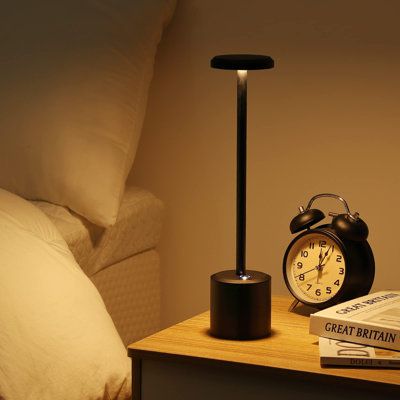 an alarm clock sitting on top of a night stand next to a book and lamp