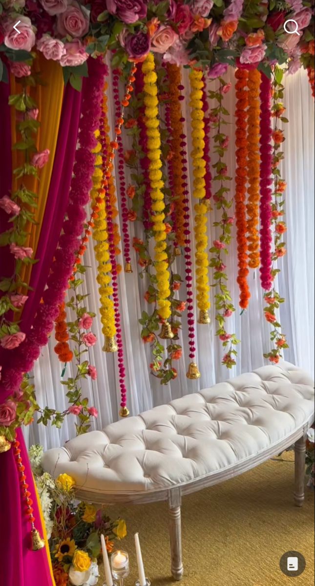 a white bench covered in lots of flowers and garlands next to a row of candles