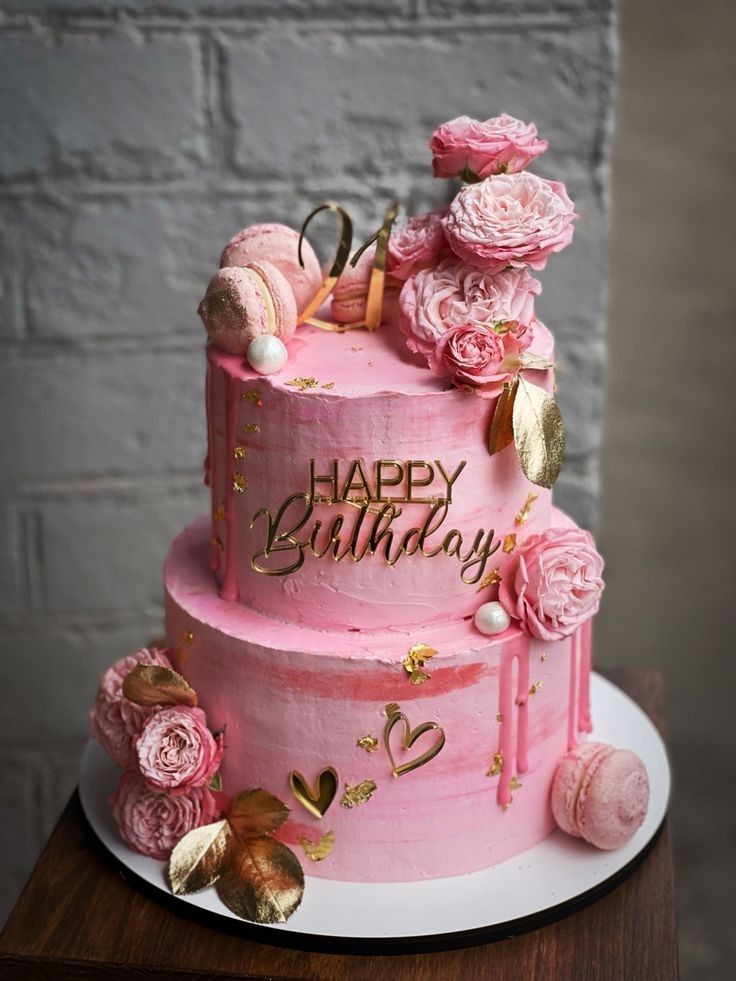 a pink birthday cake with flowers and decorations on the top is sitting on a table