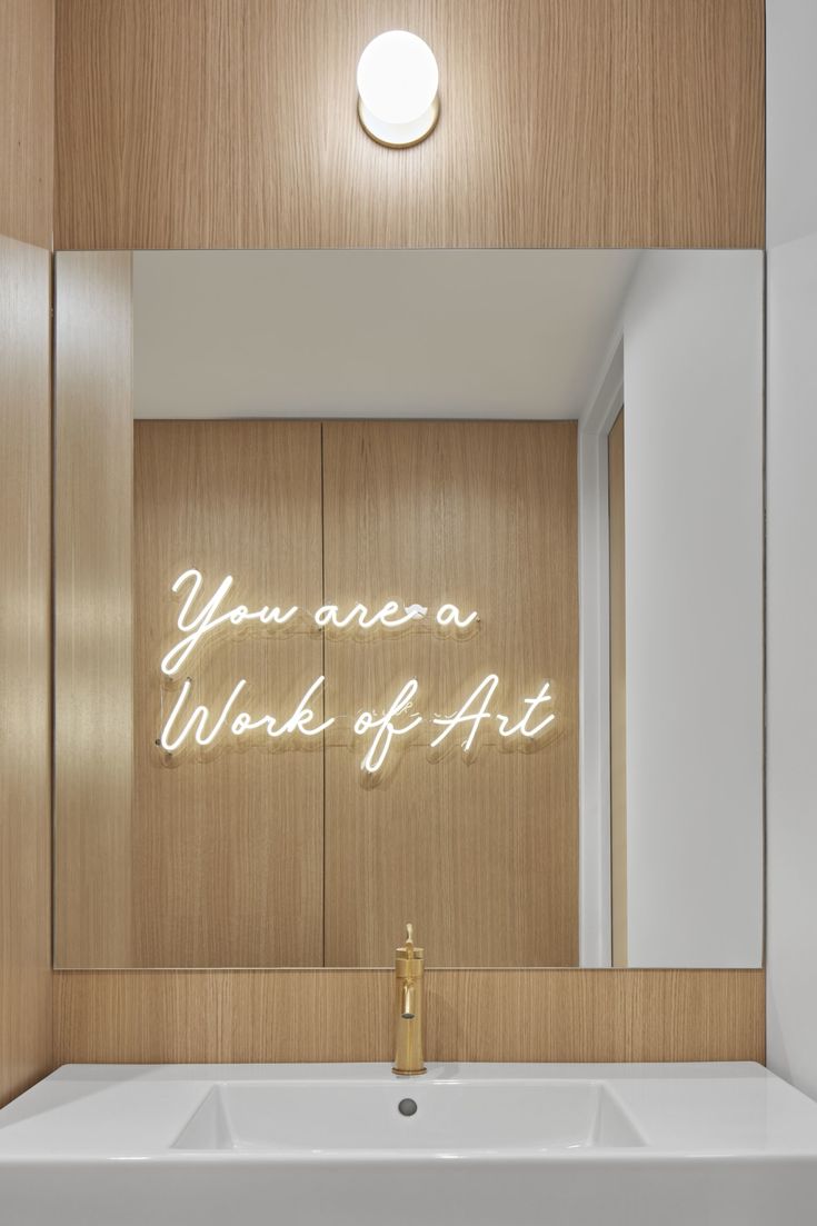 a white sink sitting under a bathroom mirror next to a wooden wall with writing on it