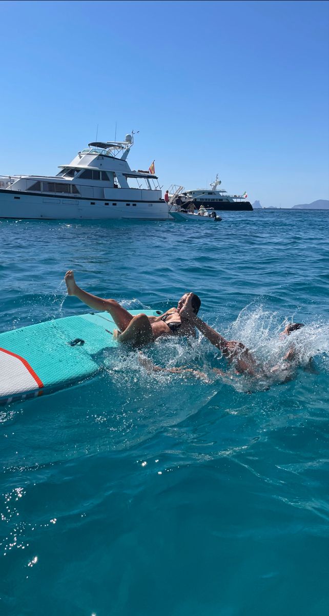 a man laying on a surfboard in the ocean next to a boat and yacht