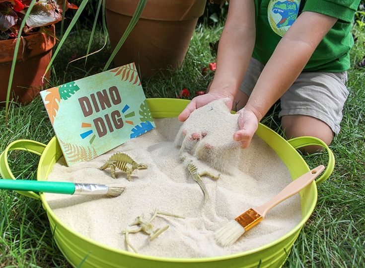 a little boy playing with sand in a green bucket filled with dinosaurs and other toys