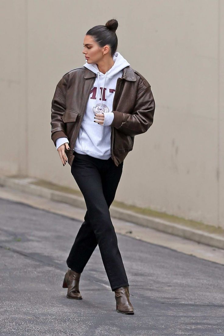 a woman walking down the street while wearing a brown jacket