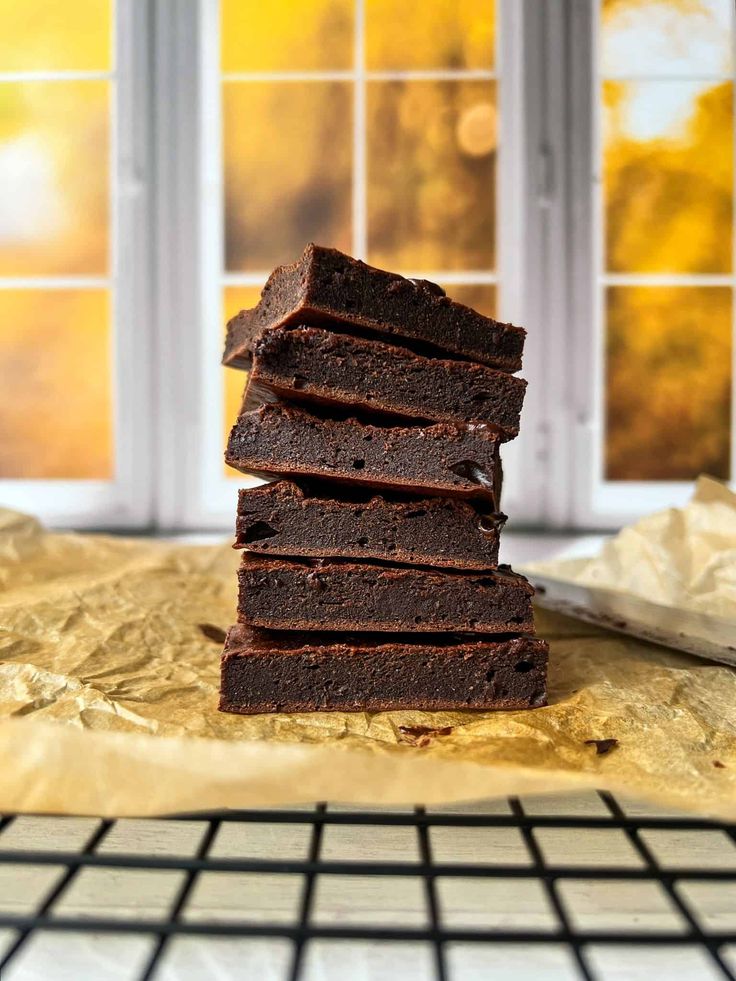 a stack of chocolate brownies sitting on top of a table next to a window