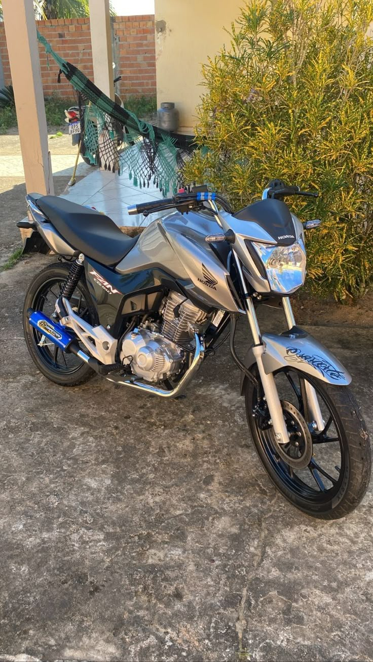 a silver and black motorcycle parked in front of a building next to shrubbery on the sidewalk