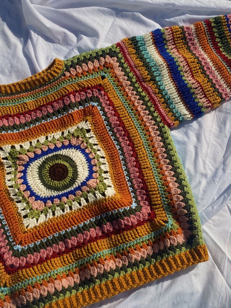 a multicolored crocheted blanket laying on top of a white bed sheet