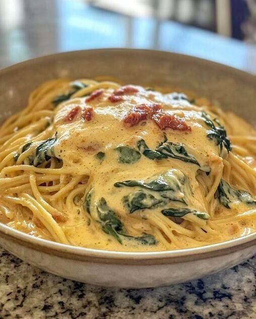 a close up of a plate of spaghetti with spinach and cheese on it in a bowl