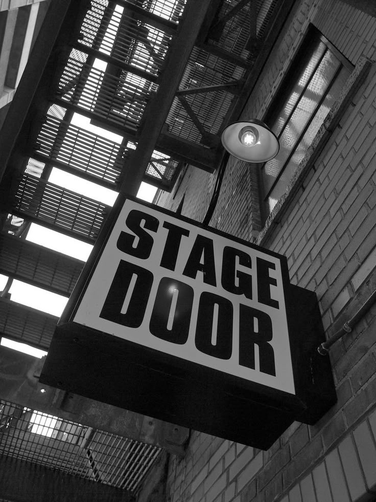 a sign hanging from the side of a brick building that says stage door on it