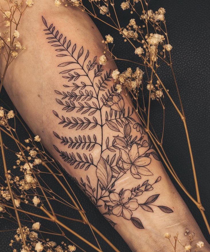 a black and white photo of a flower tattoo on the left arm, with flowers in the background