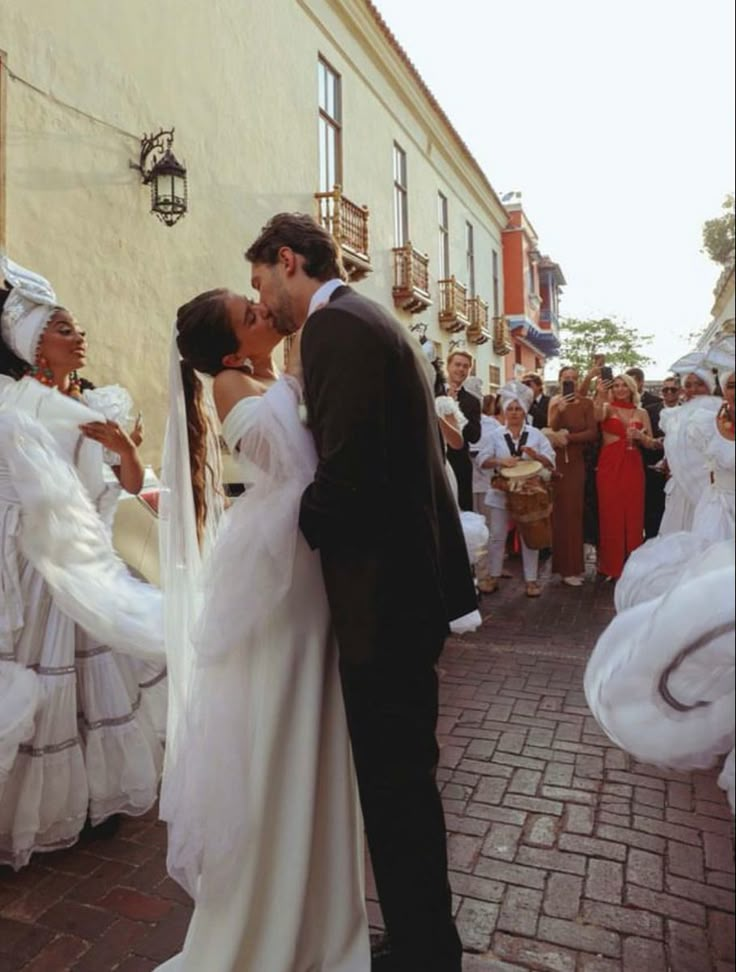 a bride and groom kissing in front of a group of people dressed in white dresses