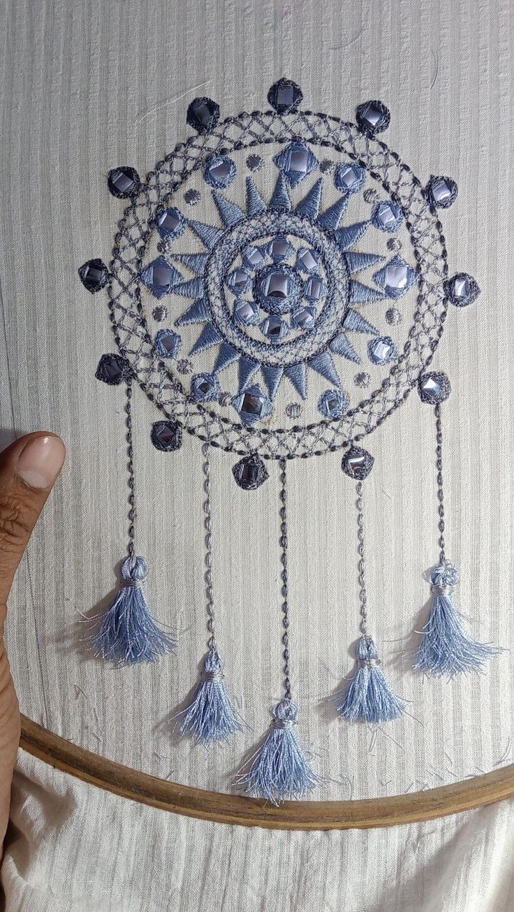 a hand holding a piece of art with tassels and beads hanging from it