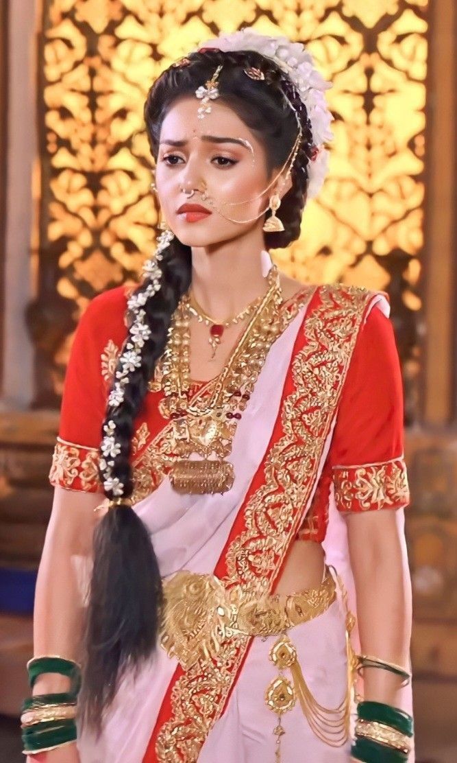 a woman in a red and white sari with gold jewelry on her head, wearing a