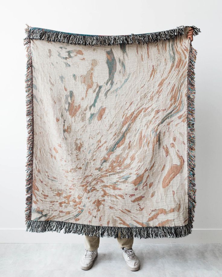 a person holding up a blanket with an image of marbled paint on it and fringes around the edges