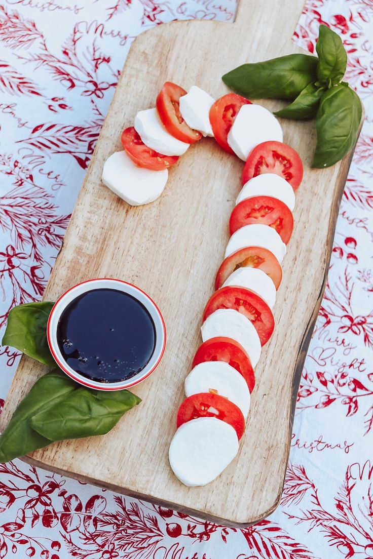 tomatoes, mozzarella and basil on a wooden cutting board with sauce in a bowl