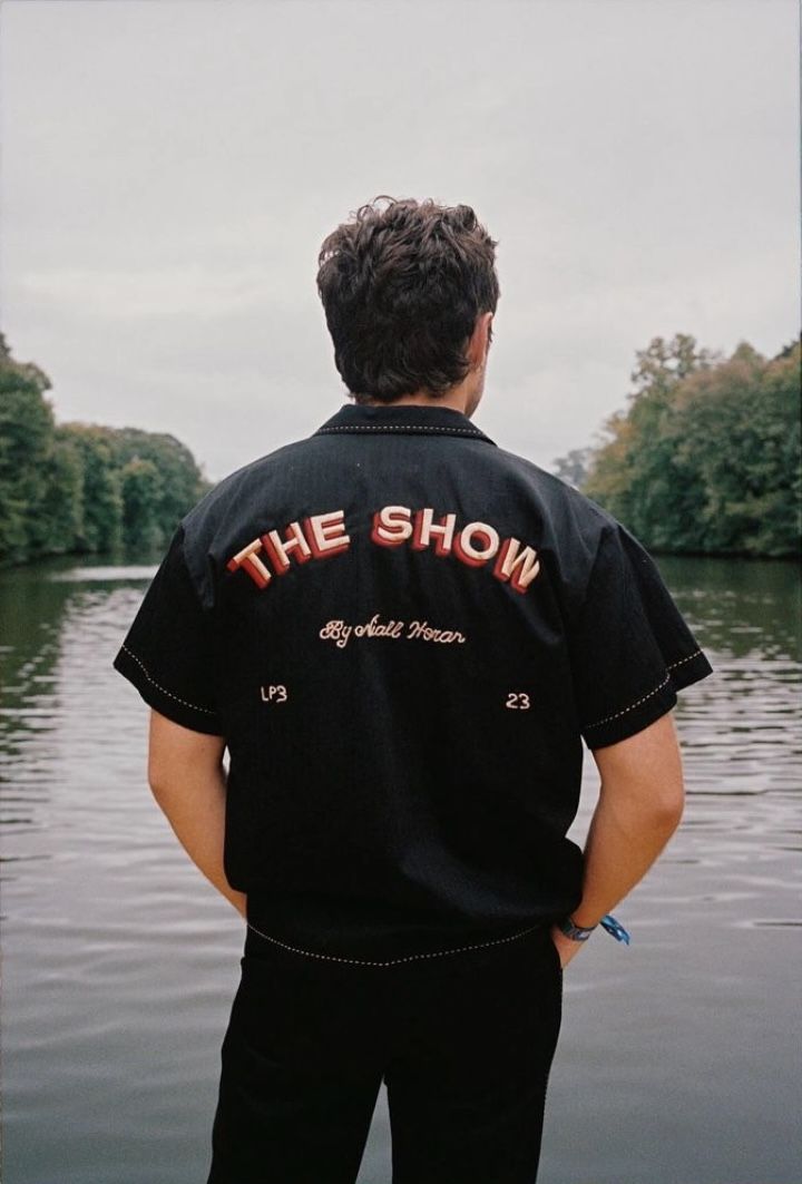 a man standing on the edge of a body of water wearing a black shirt that says the show