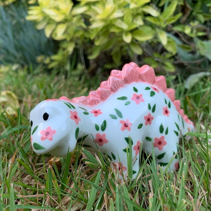 a small toy dinosaur in the grass with flowers on it's body and tail