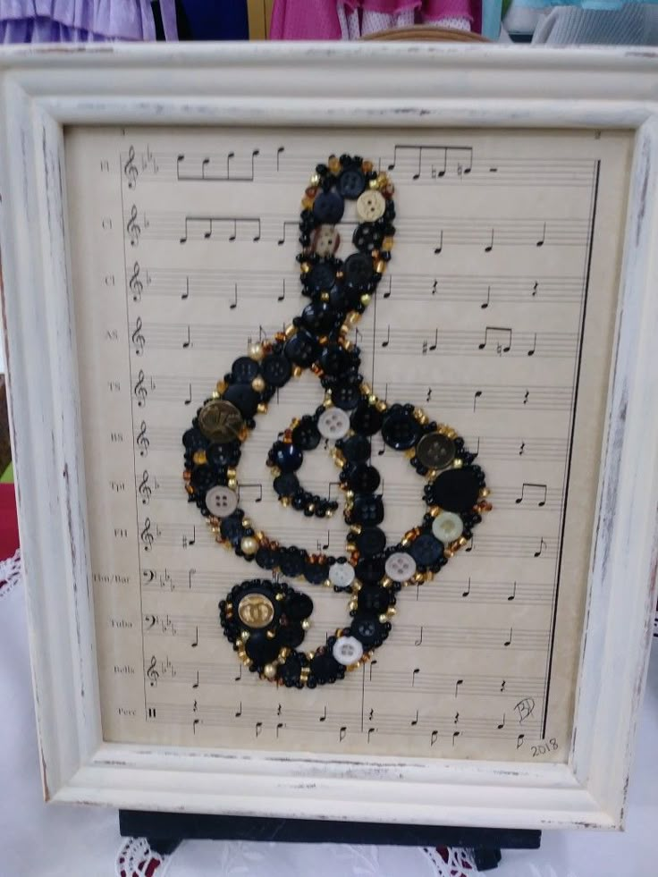 a music note made out of buttons and beads is displayed in a white frame on top of sheet music