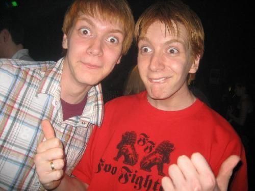 two young men posing for the camera with one pointing at the camera and the other holding his thumb up