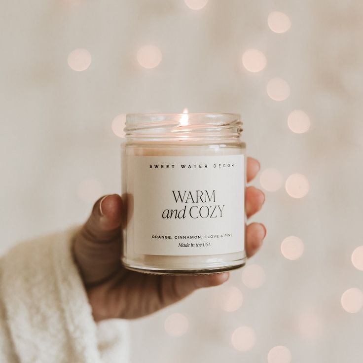 a hand holding a jar of warm and cozy candle