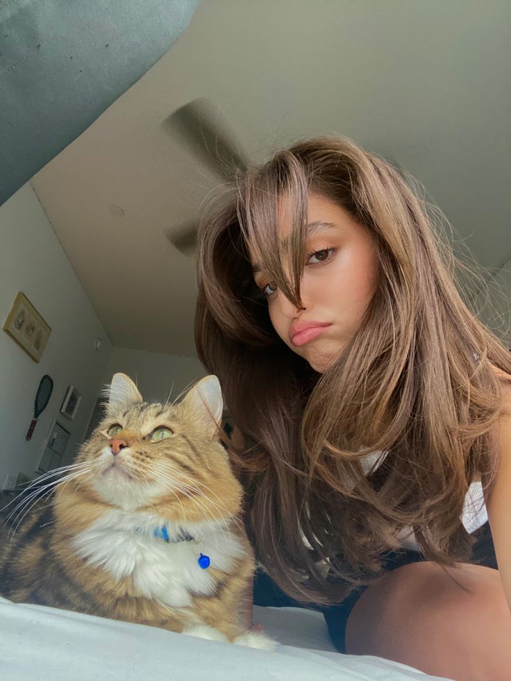 a woman laying on top of a bed next to a brown and white cat with her tongue out