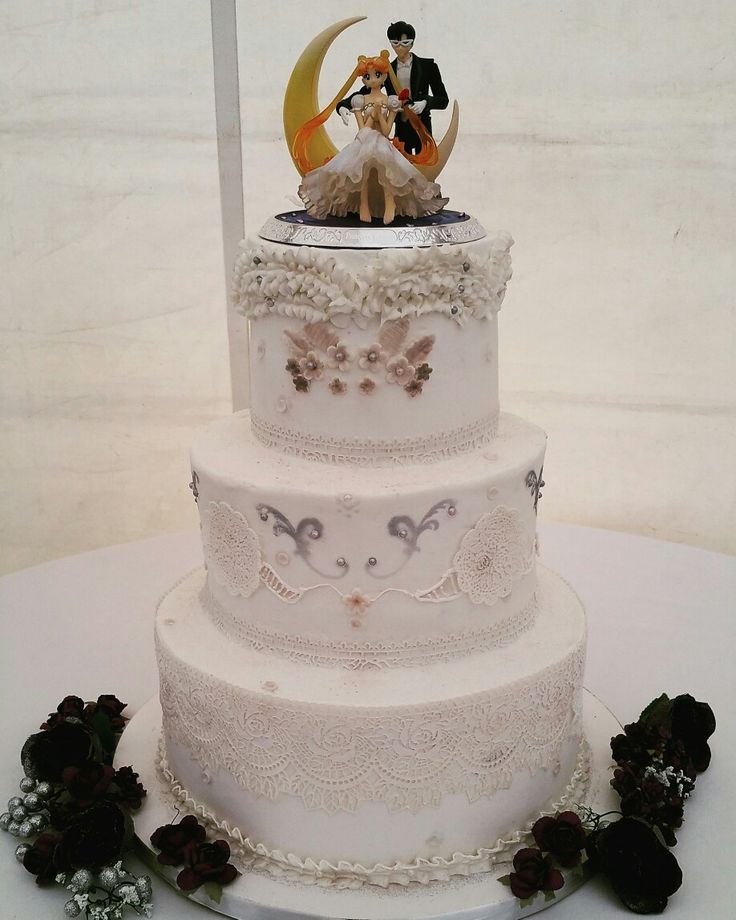 a three tiered wedding cake with figurines on top and flowers around it