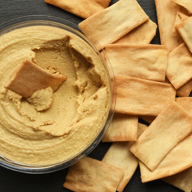 a bowl filled with hummus next to crackers on top of a black surface