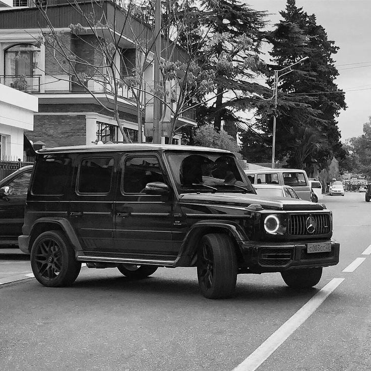 a black and white photo of a jeep parked on the side of the road in front of an apartment building