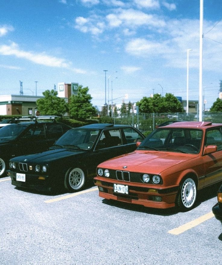 several cars parked in a parking lot with one red car and the other black bmw