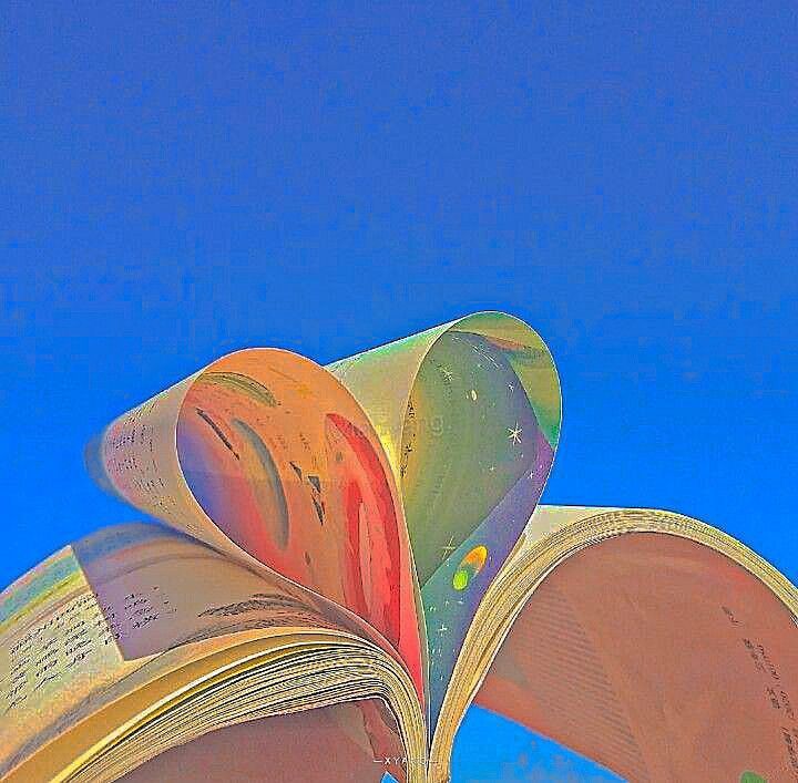 an open book sitting on top of a wooden table next to a blue sky and clouds