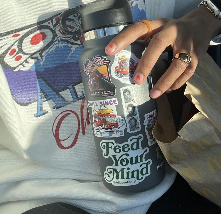 a woman holding onto a bottle that has stickers on it and the words feed your mind printed on it