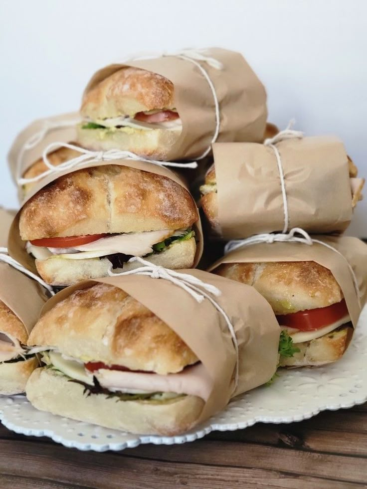 several sandwiches wrapped in brown paper on a white plate with some string around the edges