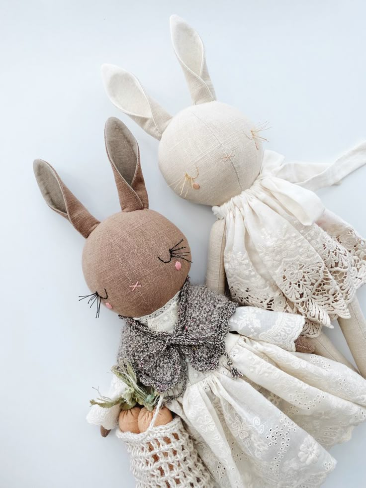 two stuffed rabbits are laying next to each other on a white tablecloth covered surface