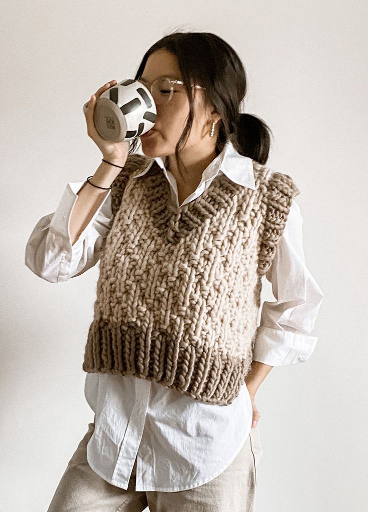 a woman drinking from a cup while wearing a knitted sweater and holding a soccer ball