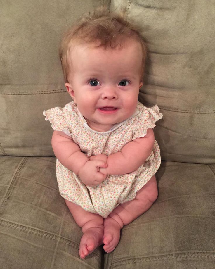 a baby is sitting on a couch with her hands in her pockets and smiling at the camera