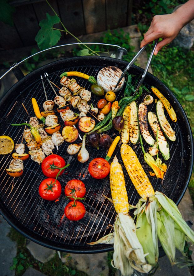 someone is grilling vegetables on the grill with tongs in their hand and there are other foods being grilled on the grill