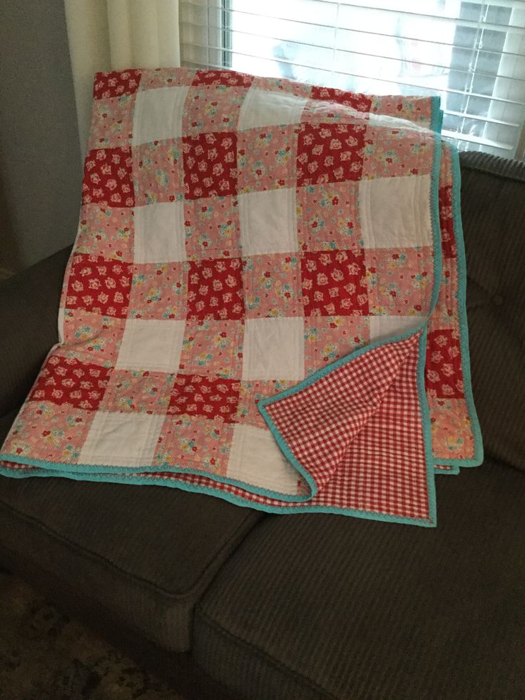 a red and white quilt sitting on top of a black couch next to a window