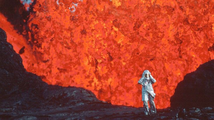 a man standing on top of a lava covered mountain next to a giant red volcano