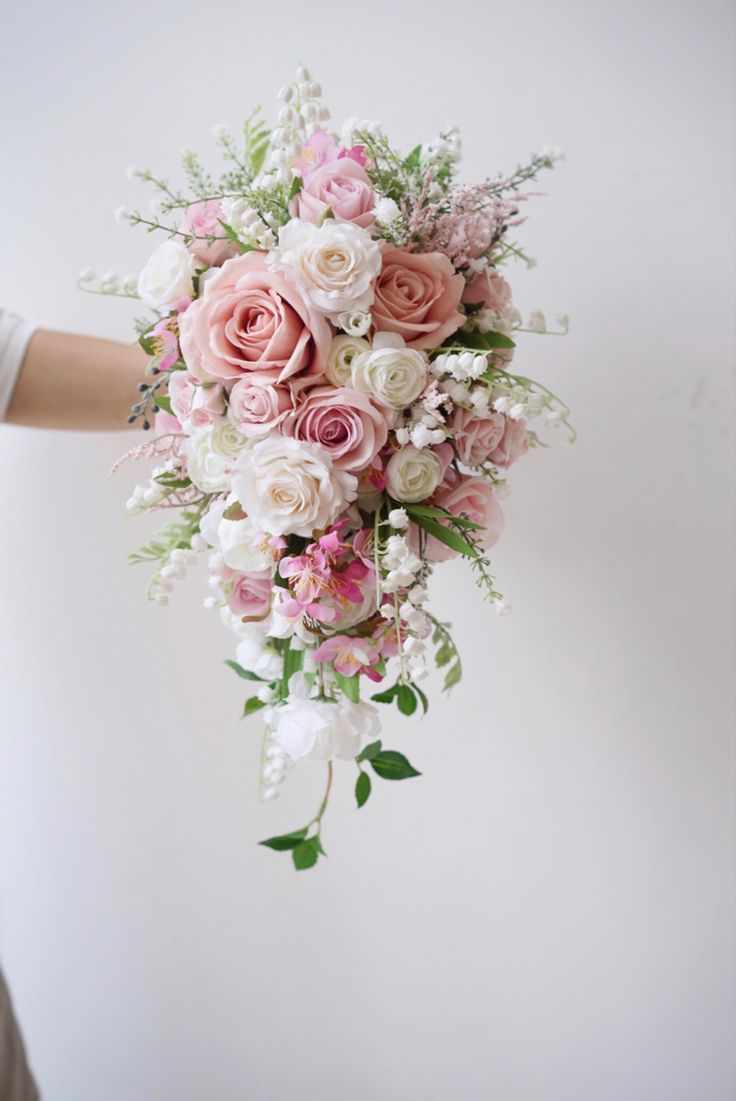 a bouquet of pink and white flowers is held by a woman's hand in front of a white wall